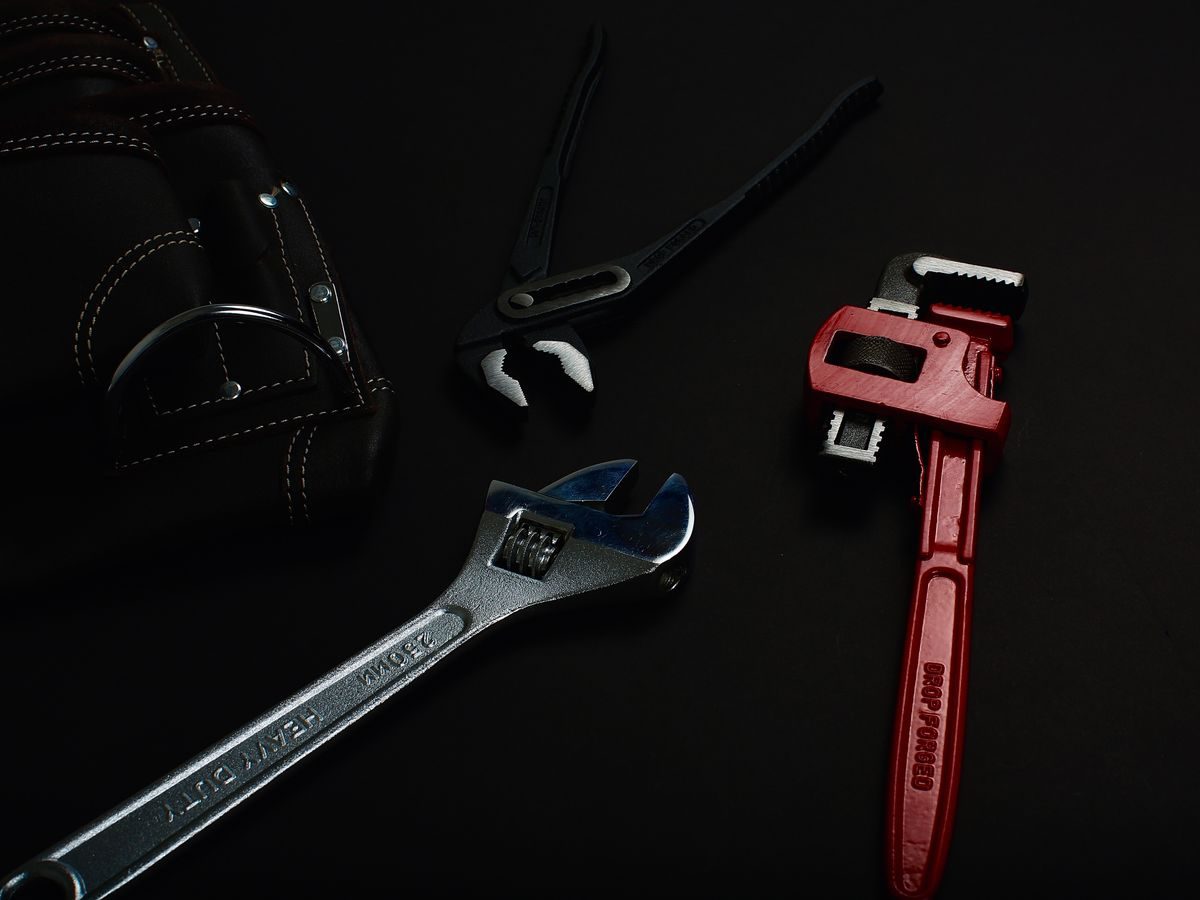 A pipe wrench, an adjustable wrench, water pump pliers and a leather tool roll laid out on a dark bench
